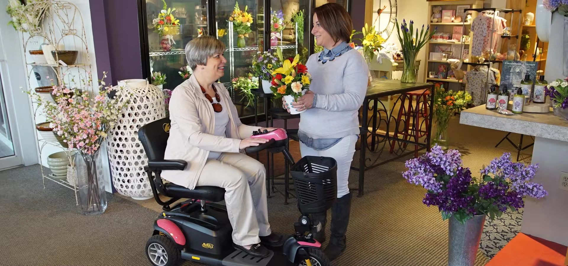 Two women in a store with flower arrangements and a mobility scooter.